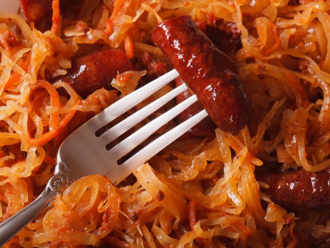 500 г кисело зеле
1 глава лук, нарязана
3 наденици
1 чаша течна готварска сметана
1 щипка черен пипер
1 щипка червен пипер
4-5 лъжици олио
1 щипка сол
1 чаша ориз
1 чаша вода