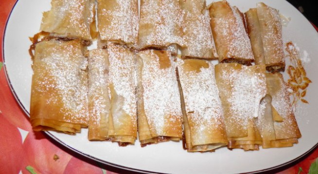 кори за баница
тиква - 500г
захар - 1ч.ч.
смлени или начукани орехи - 1 ч.ч. /може и по-щедро/
канела - 1 пакетче
лимонова кора - 1 лимон
олио - колкото е необходимо
пудра захар - за поръсване