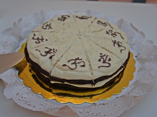 Сладка торта „Сен Жермен“ – с ванилов крем и шоколадови блатове. Вместо със захар е подсладена с растителен мед. Декорирана е със знака „Ом“.